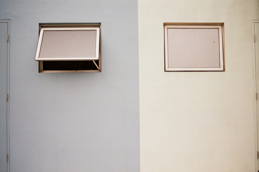 A wall with half painted grey, half cream. Each side has a small window. The grey side is open, the cream closed.